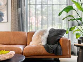Experience modern comfort in this inviting living space, featuring a luxurious tan leather sofa adorned with plush throw pillows and a cozy blanket.