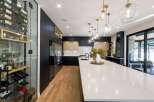 Experience luxury living in this stunning modern kitchen, featuring a sleek black cabinetry, a spacious white quartz island, and a dedicated glass-enclosed wine cellar.