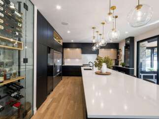 Experience luxury living in this stunning modern kitchen, featuring a sleek black cabinetry, a spacious white quartz island, and a dedicated glass-enclosed wine cellar.