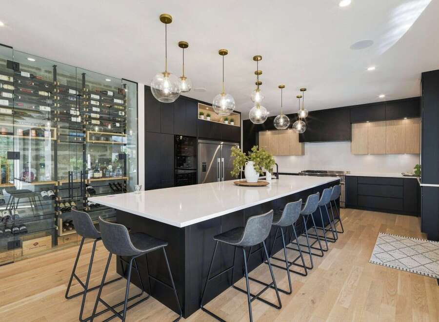 Experience luxury living in this stunning modern kitchen, featuring a sleek black island with ample seating and a breathtaking floor-to-ceiling glass wine cellar.