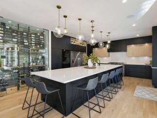 Experience luxury living in this stunning modern kitchen, featuring a sleek black island with ample seating and a breathtaking floor-to-ceiling glass wine cellar.
