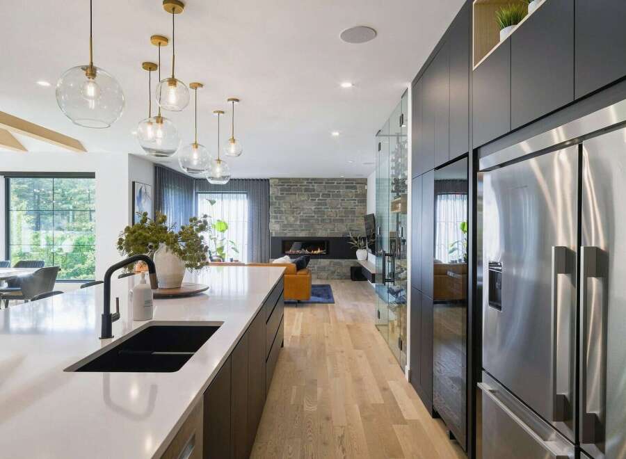 Experience modern luxury in this open-concept living space, featuring a sleek white island with a black sink and faucet, complemented by a stunning stone fireplace in the living area.