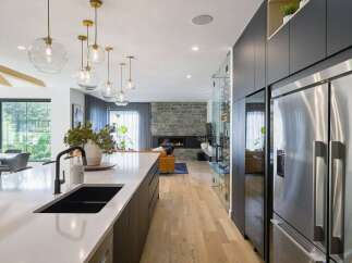 Experience modern luxury in this open-concept living space, featuring a sleek white island with a black sink and faucet, complemented by a stunning stone fireplace in the living area.