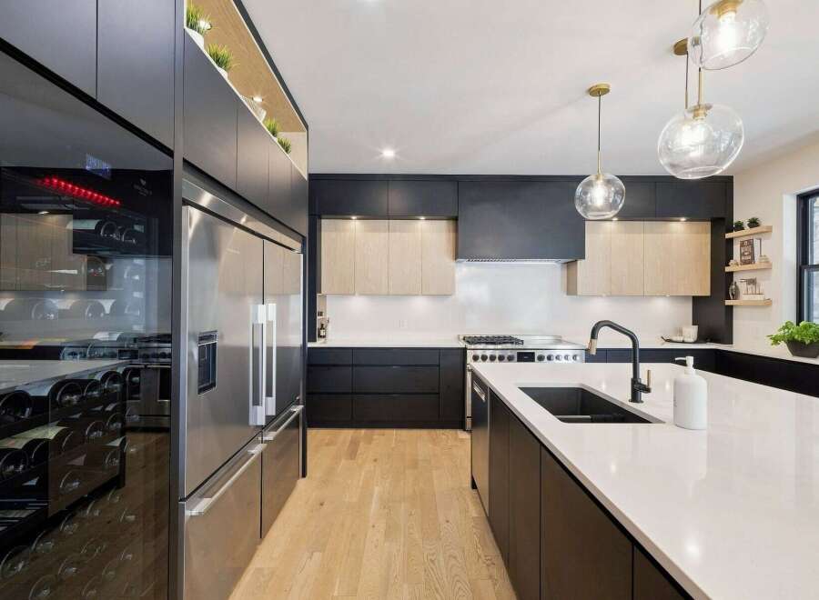 Experience modern luxury in this stunning kitchen, featuring sleek dark cabinetry, a spacious island with a waterfall countertop, and a professional-grade stainless steel refrigerator.