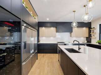 Experience modern luxury in this stunning kitchen, featuring sleek dark cabinetry, a spacious island with a waterfall countertop, and a professional-grade stainless steel refrigerator.