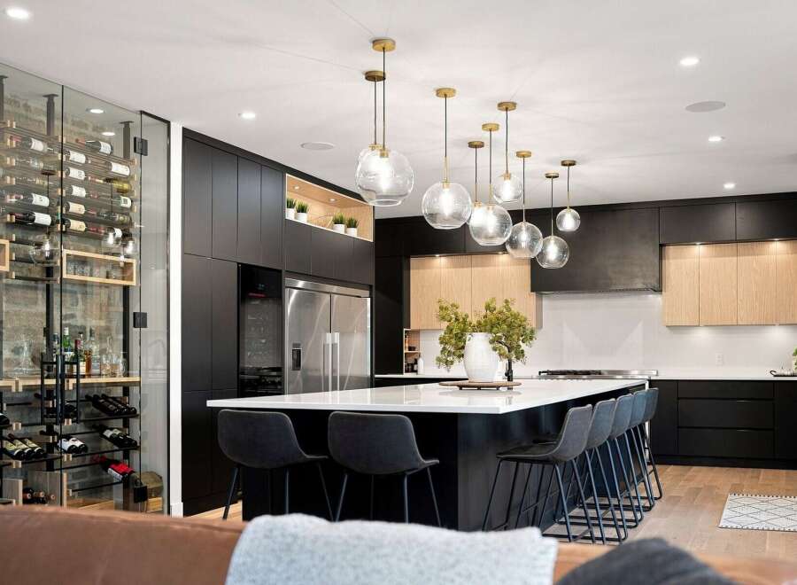 Experience luxury living in this modern kitchen featuring a stunning glass-encased wine cellar and a spacious island with bar seating.