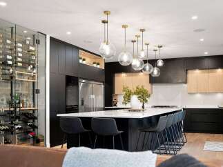 Experience luxury living in this modern kitchen featuring a stunning glass-encased wine cellar and a spacious island with bar seating.