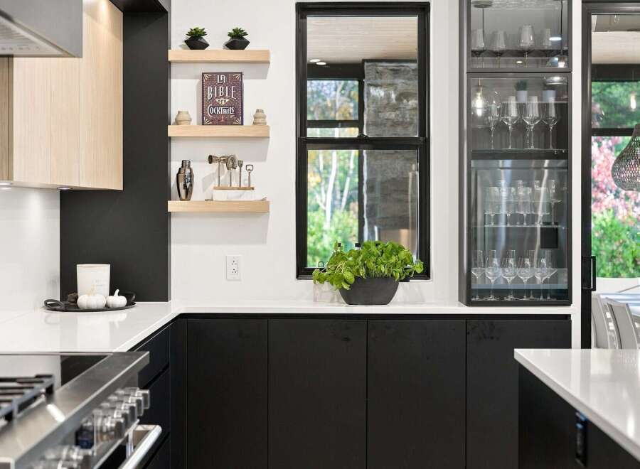 This modern kitchen boasts sleek black cabinetry contrasted with light wood accents and a pristine white countertop.