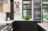 This modern kitchen boasts sleek black cabinetry contrasted with light wood accents and a pristine white countertop.