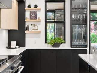 This modern kitchen boasts sleek black cabinetry contrasted with light wood accents and a pristine white countertop.