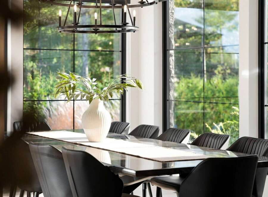 Experience elegant dining in this sophisticated space, featuring a sleek, dark dining table adorned with a textured runner and a striking white vase with greenery.