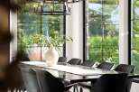 Experience elegant dining in this sophisticated space, featuring a sleek, dark dining table adorned with a textured runner and a striking white vase with greenery.