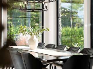 Experience elegant dining in this sophisticated space, featuring a sleek, dark dining table adorned with a textured runner and a striking white vase with greenery.