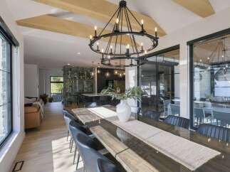 Experience modern luxury in this spacious dining area, featuring a stunning double-ring chandelier and exposed wooden beams that add architectural interest.