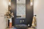 This modern bathroom features a sleek, dark vessel sink paired with elegant brass faucets.