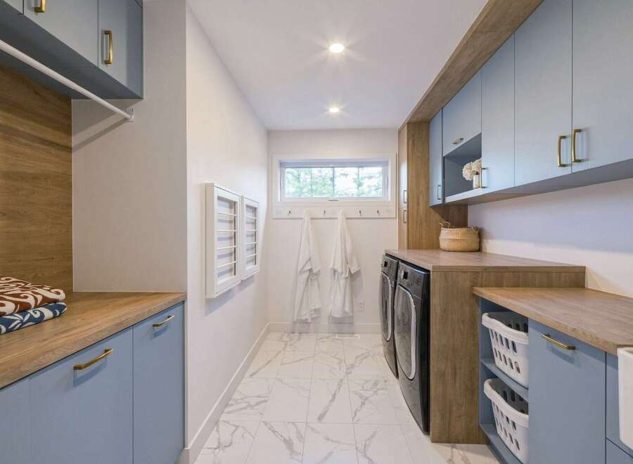 This modern laundry room boasts a stylish and functional design, featuring light blue cabinetry with elegant gold hardware.