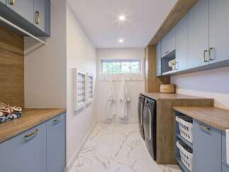 This modern laundry room boasts a stylish and functional design, featuring light blue cabinetry with elegant gold hardware.
