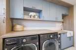 This modern laundry room boasts a sleek design with light blue cabinetry and warm wood accents.
