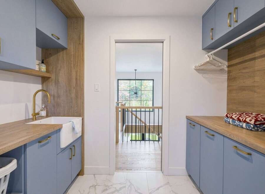 This modern laundry room boasts a stylish design with light blue cabinetry and warm wood accents.