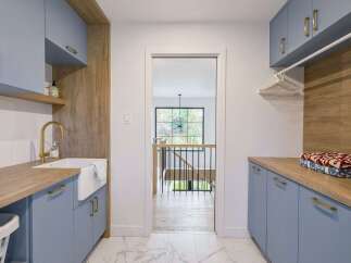 This modern laundry room boasts a stylish design with light blue cabinetry and warm wood accents.