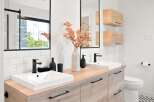 This modern bathroom features a double vanity with clean white sinks and sleek black faucets, complemented by warm wood cabinetry and a subway tile backsplash.