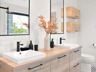 This modern bathroom features a double vanity with clean white sinks and sleek black faucets, complemented by warm wood cabinetry and a subway tile backsplash.