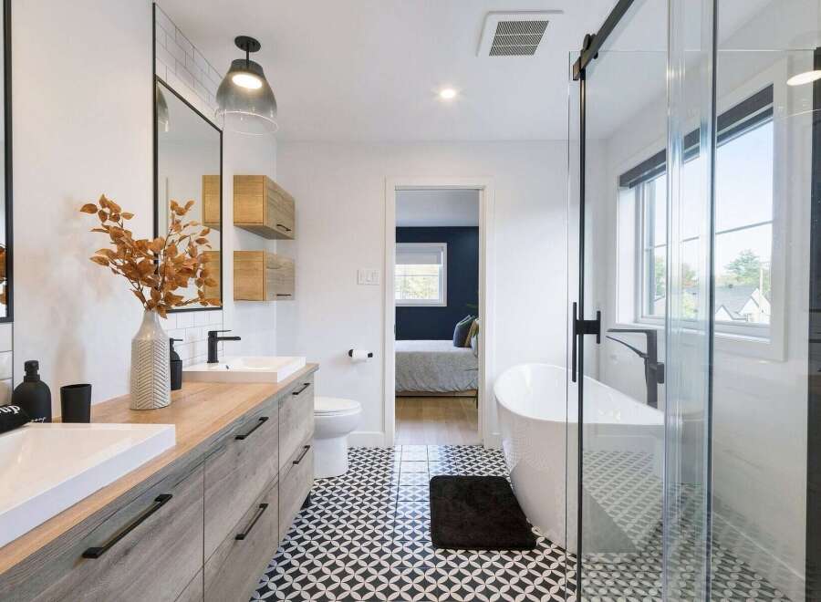 This modern bathroom features a double vanity with a wood-look finish and sleek black hardware, complemented by a striking geometric tile floor.
