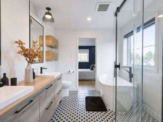 This modern bathroom features a double vanity with a wood-look finish and sleek black hardware, complemented by a striking geometric tile floor.