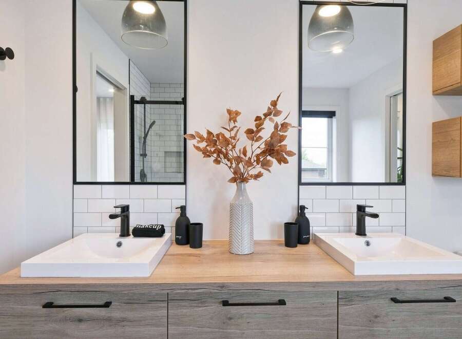 This modern bathroom features a double vanity with two sleek white sinks and black faucets, set against a backdrop of white subway tiles.