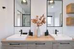 This modern bathroom features a double vanity with two sleek white sinks and black faucets, set against a backdrop of white subway tiles.