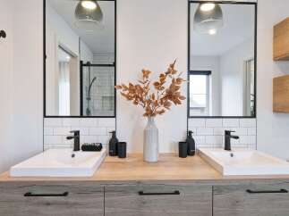 This modern bathroom features a double vanity with two sleek white sinks and black faucets, set against a backdrop of white subway tiles.