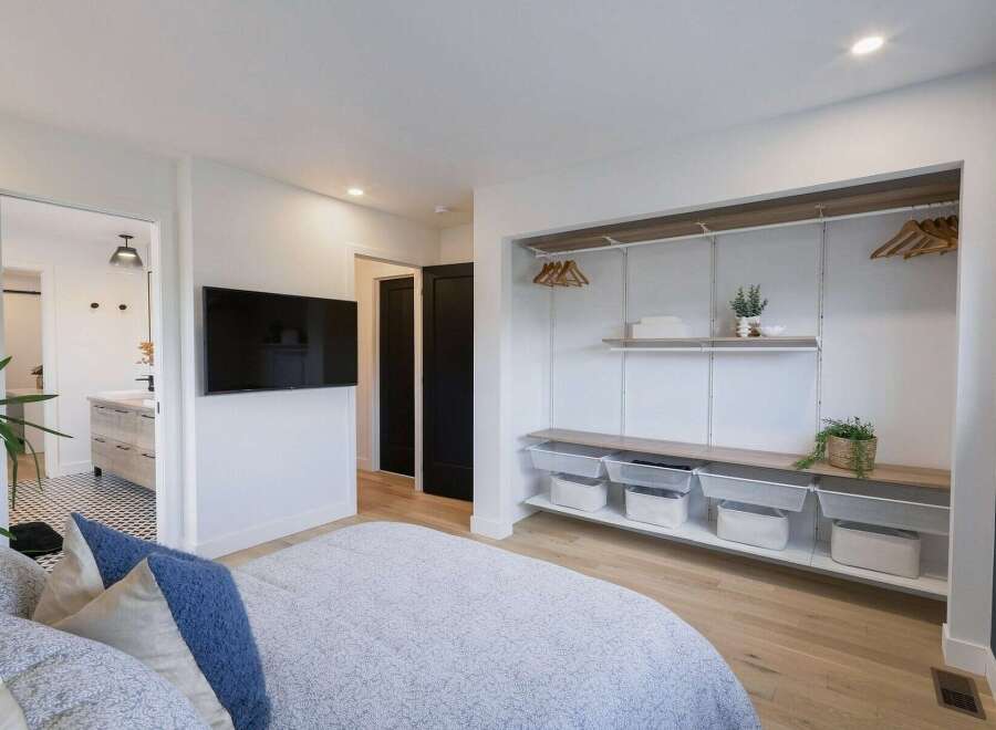 This modern bedroom features a sleek wall-mounted TV and an open-concept closet system with ample shelving and storage baskets.