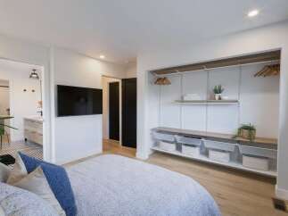 This modern bedroom features a sleek wall-mounted TV and an open-concept closet system with ample shelving and storage baskets.