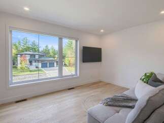 Experience modern living in this spacious room featuring a large picture window that offers a stunning view of the contemporary home and its manicured lawn.