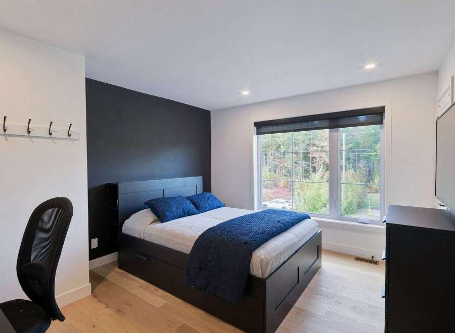 This modern bedroom features a sleek black platform bed with ample storage drawers, complemented by a dark accent wall and crisp white walls.