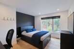 This modern bedroom features a sleek black platform bed with ample storage drawers, complemented by a dark accent wall and crisp white walls.