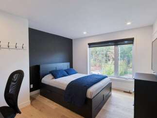 This modern bedroom features a sleek black platform bed with ample storage drawers, complemented by a dark accent wall and crisp white walls.