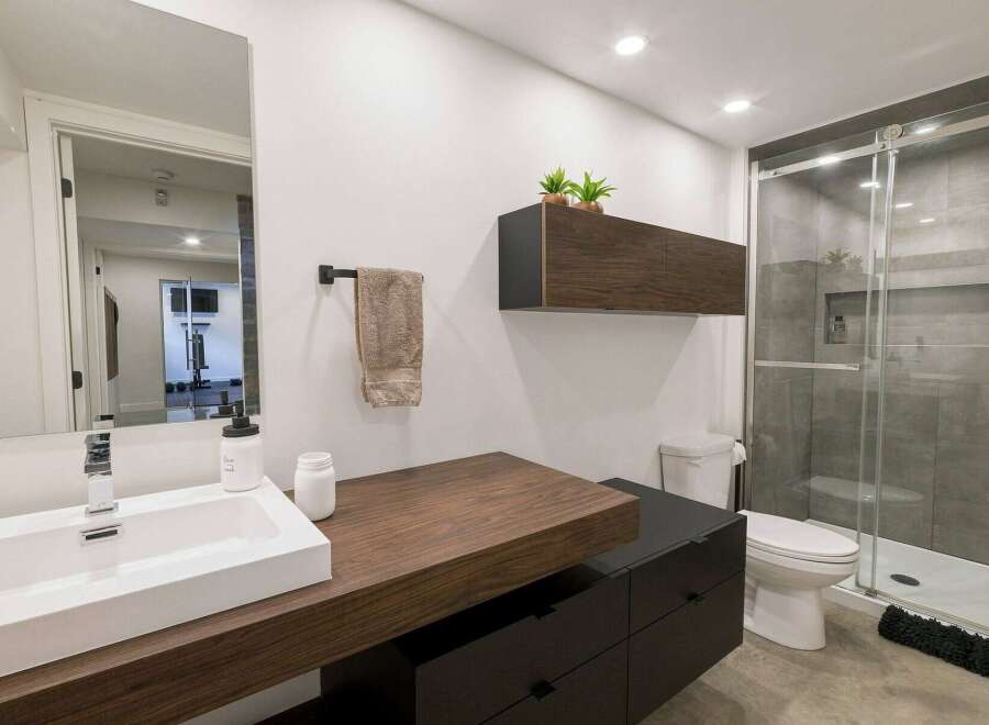 This modern bathroom features a sleek floating vanity with a white rectangular sink and a chrome faucet, complemented by dark wood cabinetry.