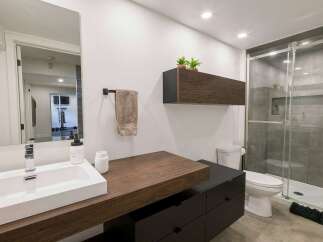 This modern bathroom features a sleek floating vanity with a white rectangular sink and a chrome faucet, complemented by dark wood cabinetry.