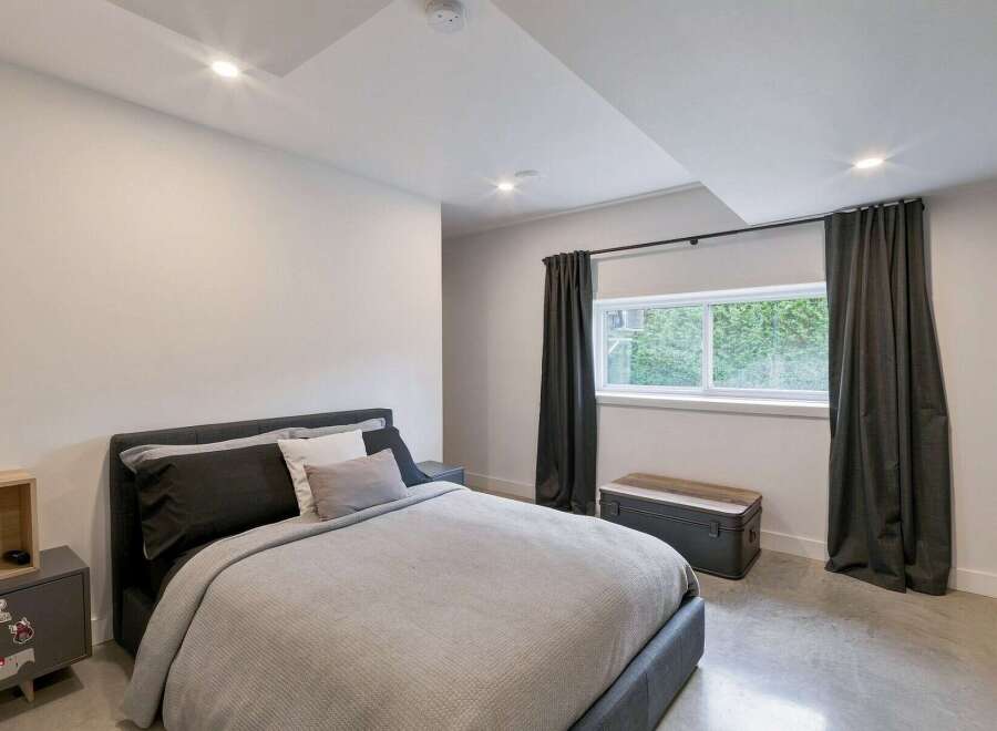 This modern bedroom features a comfortable bed with dark gray and white linens, complemented by a matching nightstand with a wooden accent.