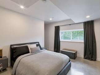 This modern bedroom features a comfortable bed with dark gray and white linens, complemented by a matching nightstand with a wooden accent.