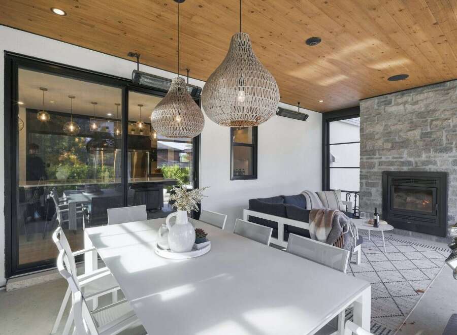 Experience seamless indoor-outdoor living in this beautifully appointed covered patio, featuring a spacious dining area and a cozy lounge space with a stone fireplace.