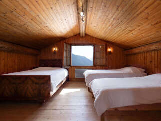 Experience rustic charm in this attic bedroom, featuring three comfortable beds and a stunning mountain view through the open window.