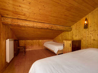 Experience rustic charm in this cozy attic bedroom, featuring warm wooden paneling and a sloped ceiling with exposed beams.