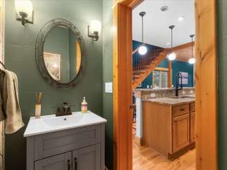 This charming bathroom features a stylish gray vanity with a white countertop and sink, complemented by a decorative oval mirror and wall sconces.