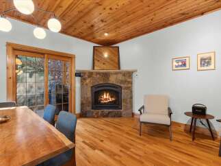 Cozy up by the stone fireplace in this inviting living space, featuring a warm wood-paneled ceiling and gleaming hardwood floors.