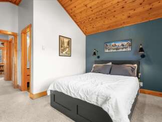 Experience cozy mountain living in this charming bedroom featuring a vaulted wood-paneled ceiling and a striking teal accent wall.