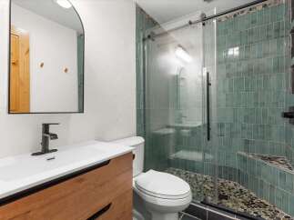 This modern bathroom features a sleek vanity with a wooden finish and a waterfall faucet, complemented by a stylish arched mirror.