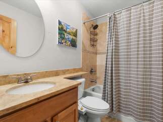 This bathroom features a spacious vanity with a granite countertop and an undermount sink, complemented by a large round mirror.