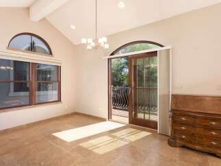 This elegant room features a high vaulted ceiling with a modern chandelier, complemented by a large arched window and a sliding glass door leading to an outdoor balcony.